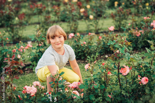 Summer portrait of cute little boy playing in rose garden