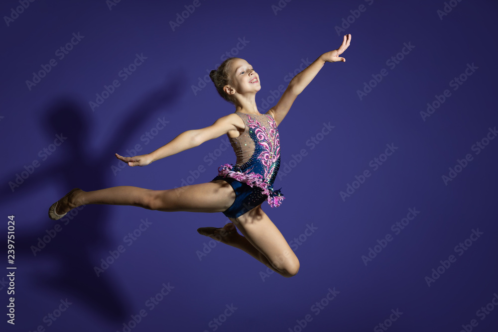 girl gymnast performs the jump. Frozen motion. Violet background. A child in a bathing suit for rhythmic gymnastics