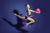 girl gymnast performs a jump with the ball. Frozen motion. Violet background. A child in a bathing suit for rhythmic gymnastics.