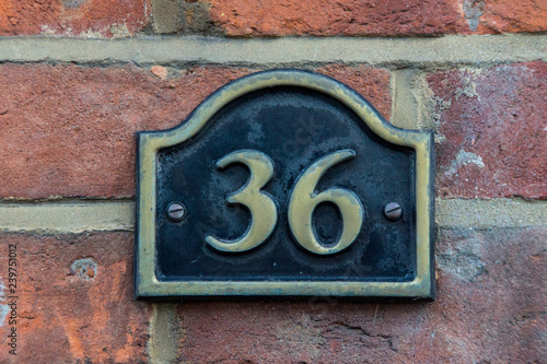 The house number 36 in brass on a red brick wall,