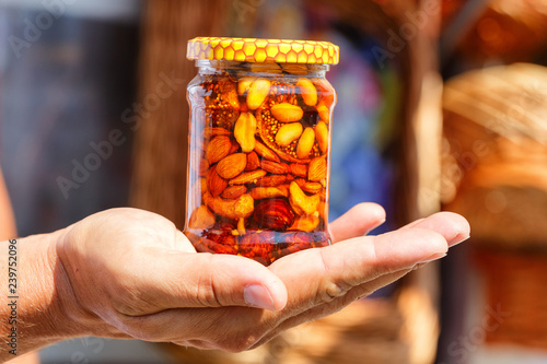 useful sweetness, nuts in honey in a glass jar, a man holds in his hand.