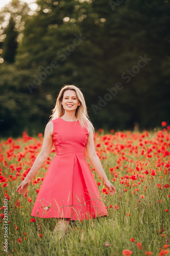 Beautiful woman enjoying nice day in poppy field, wearing pink dress