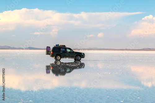 off road vehicle over a reflective salt flat ground. Clouds and sky, Uyuni, Bolivia.