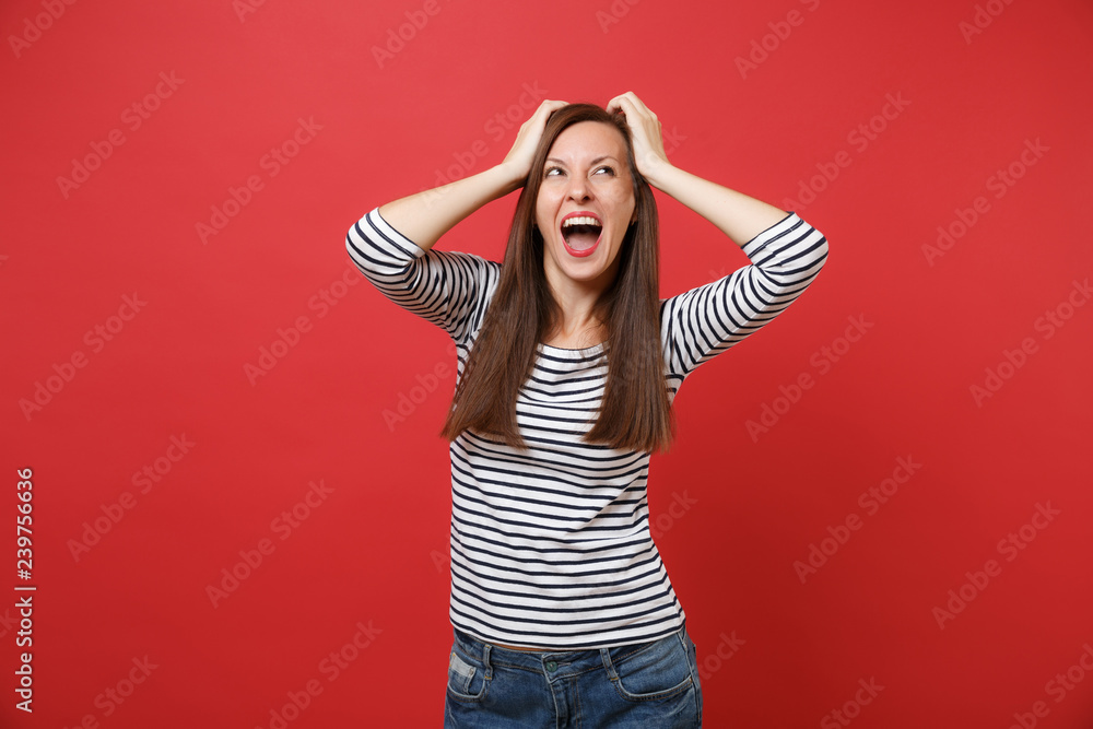 Portrait of cheerful young woman in casual striped clothes clinging to head looking up screaming isolated on bright red wall background. People sincere emotions, lifestyle concept. Mock up copy space. Portrait of cheerful young woman in casual striped clothes clinging to head looking up screaming isolated on bright red wall background. People sincere emotions, lifestyle concept. Mock up copy space.