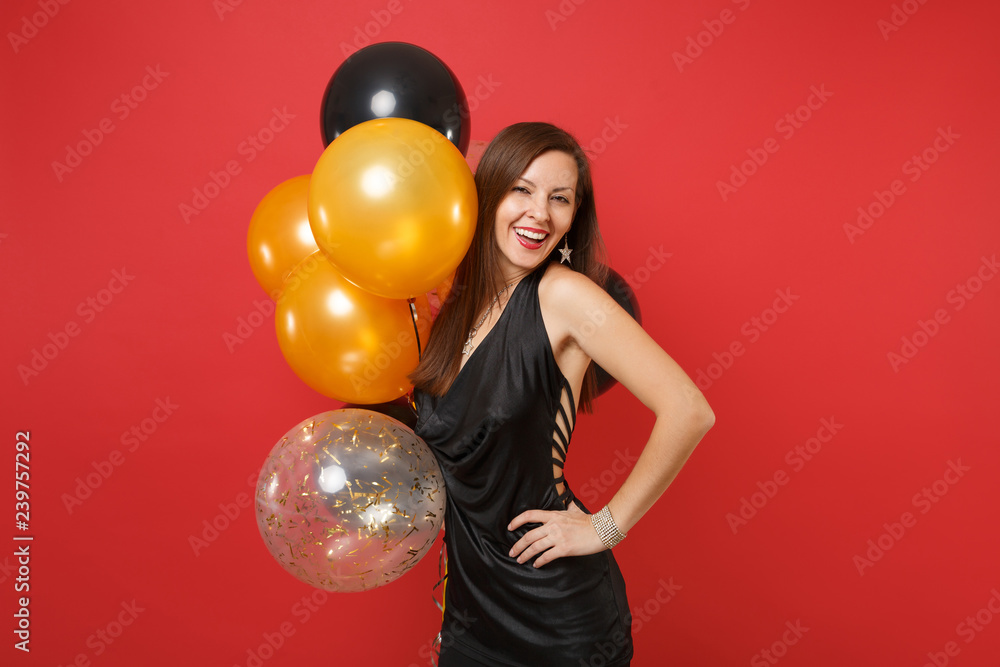 Fototapeta premium Attractive young girl in little black dress celebrating holding air balloons isolated on red background. St. Valentine's International Women's Day Happy New Year birthday mockup holiday party concept.