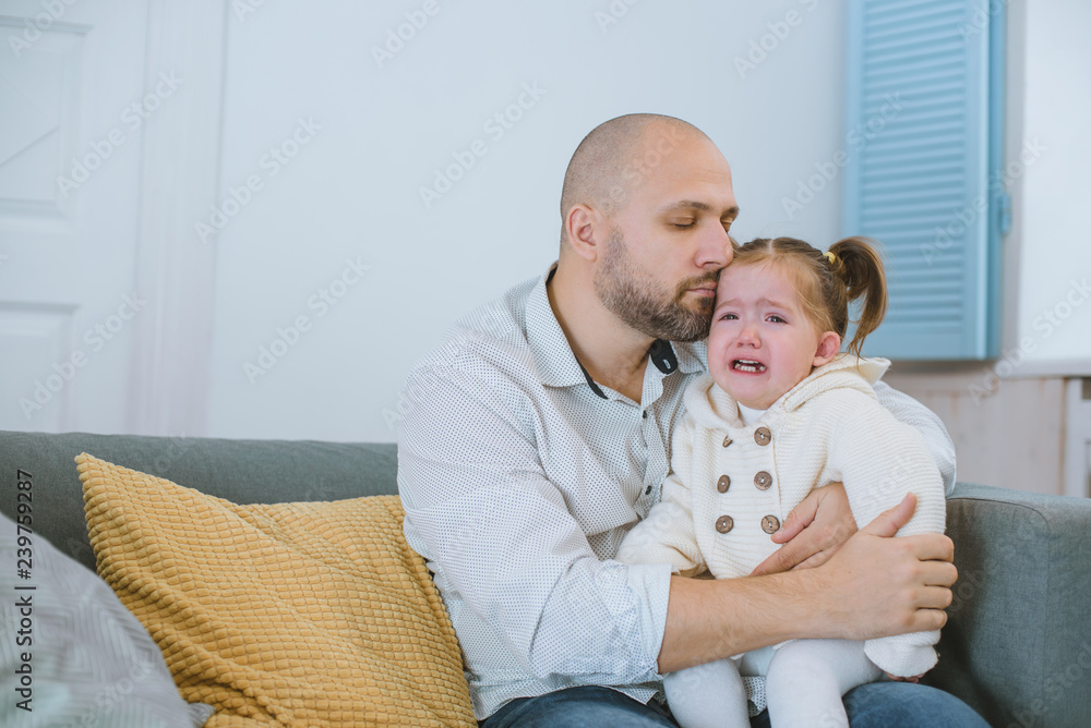 The toddler girl cries in her father's arms. The toddler girl cries in her father's arms.