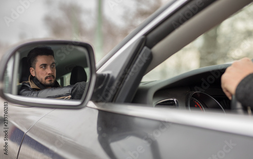 Handsome young man driving car photographed in rear view mirror