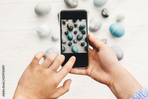 Wallpaper Mural Hands holding phone and making photo of stylish easter flat lay of eggs on rustic white wood. Blogging concept. Happy Easter. Modern easter eggs painted with natural dye in grey Torontodigital.ca