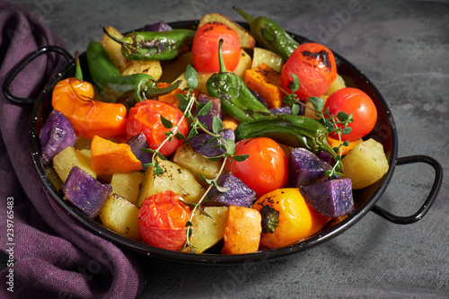 Rustic, oven baked vegetables in baking dish. Seasonal vegetarian vegan meal on dark background with linen towel
