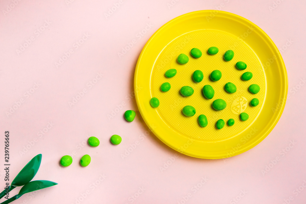 Yellow plastic plate with a path of sweets with green spoons on a pink background Yellow plastic plate with a path of sweets with green spoons on a pink background