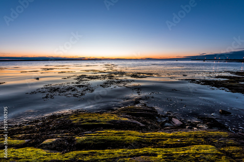 Twilight, dusk in Rimouski, Quebec, Saint Lawrence river, Gaspesie, Canada with rocks, boulders, rocky beach, turquoise water, sun reflection seaweed blue sky