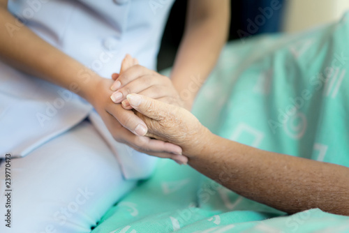 Nurse sitting on a hospital bed next to an older woman helping hands  care for the elderly concept