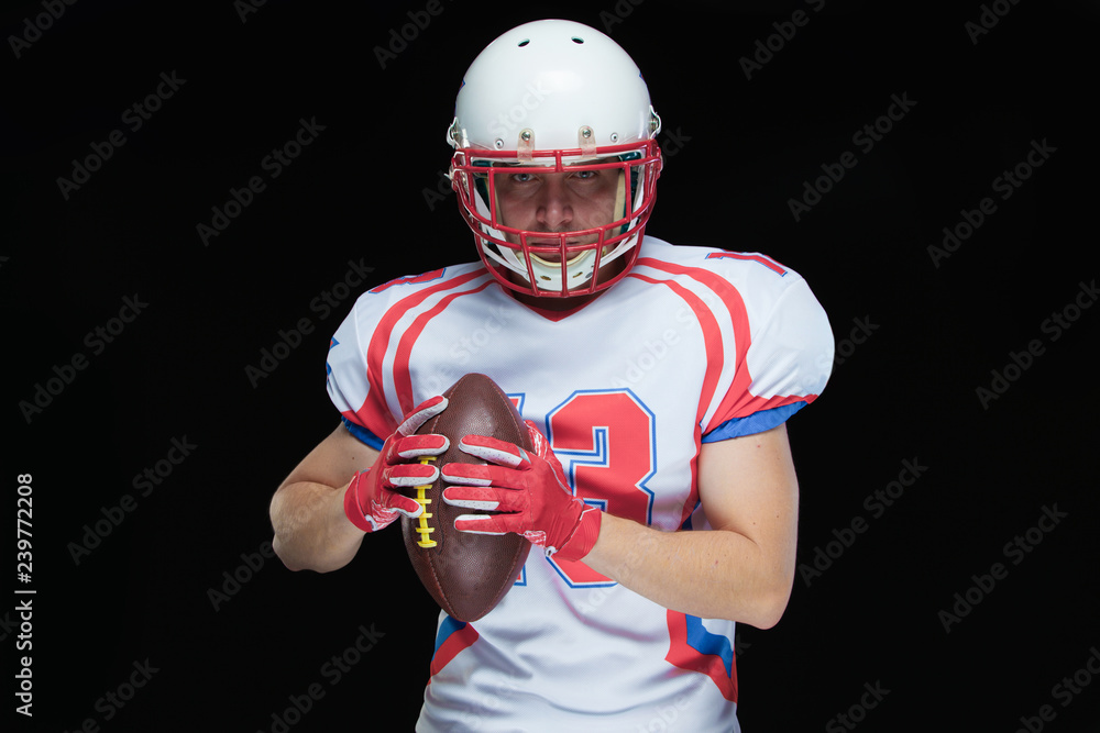 American football player wearing helmet posing with ball on black background American football player wearing helmet posing with ball on black background