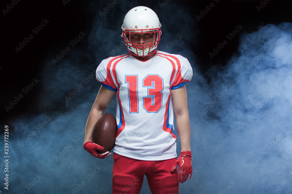 Front view portrait of american football player wearing helmet with ball against white smoke Front view portrait of american football player wearing helmet with ball against white smoke