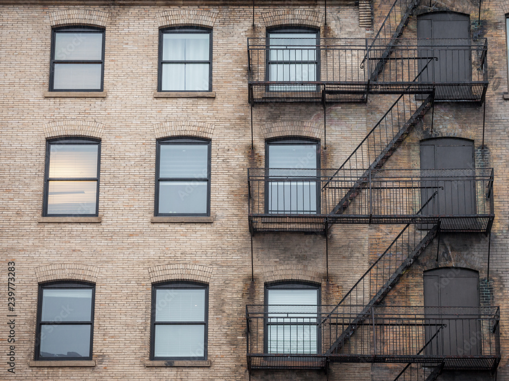 Fototapeta premium Fire escape stairs and ladder, in metal, on a typical North American old brick building from the Old Montreal, Quebec, Canada. These stairs, made for emergency, are symbolic of the architecture