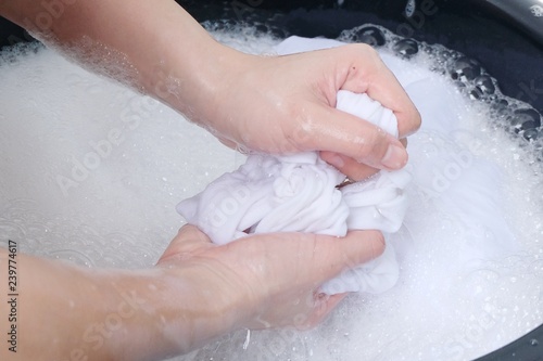 A woman washes clothes by hand in the soapy water, isolated on white background.