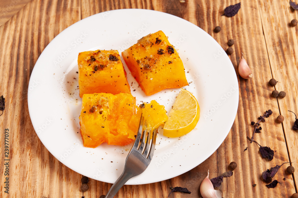 Baked pumpkin with garlic, rosemary and spices on a plate on the table. Appetizer. Garnish. Vegetarian food Baked pumpkin with garlic, rosemary and spices on a plate on the table. Appetizer. Garnish. Vegetarian food