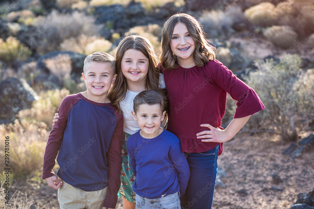 Beautiful Portrait of smiling happy kids outdoors. Four siblings standing together for a cute picture. One teen girl and three younger kids Beautiful Portrait of smiling happy kids outdoors. Four siblings standing together for a cute picture. One teen girl and three younger kids