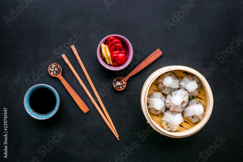 Dinner in Chinese restaurant with dim sum, sticks and tea on black background top view