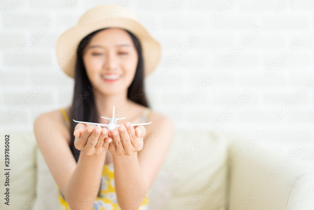Asian woman's hand flying toy plane .Beautiful young woman smiling  planning  vacation summer trip.she think  and sitting sofa on brick background.