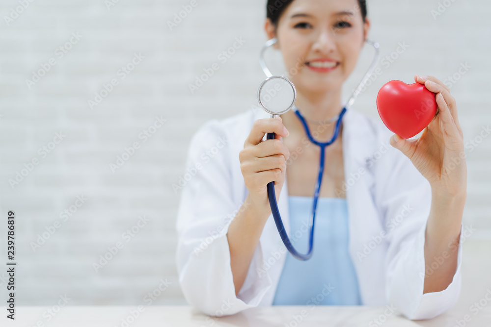 Young woman doctor holding a red heart, standing on brick wall background Young woman doctor holding a red heart, standing on brick wall background