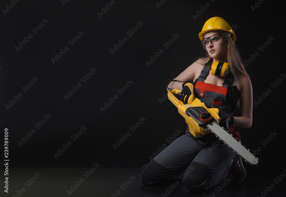 girl in overalls posing with an electric saw