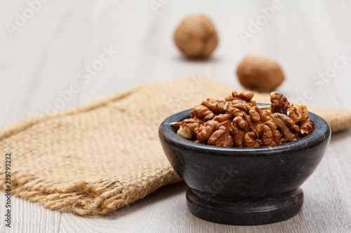 Walnuts in stone bowl with sackcloth on a wooden background.