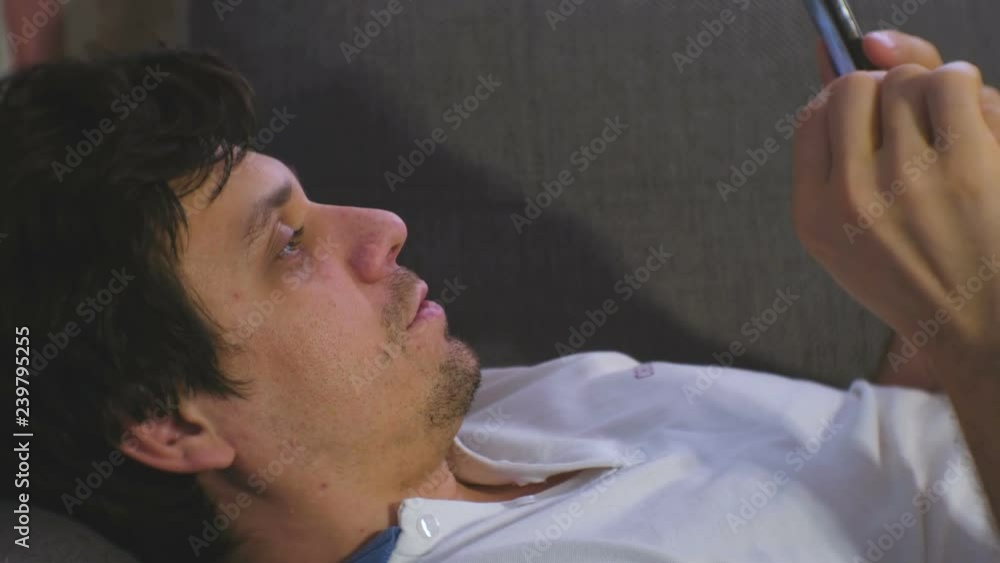 Man talks video chat on mobile phone laying on the sofa. Man talks video chat on mobile phone laying on the sofa.