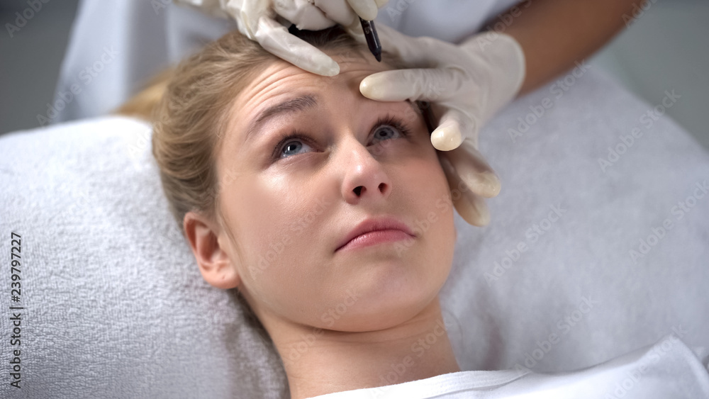 Experienced cosmetologist marking position of wrinkles on girls forehead Experienced cosmetologist marking position of wrinkles on girls forehead