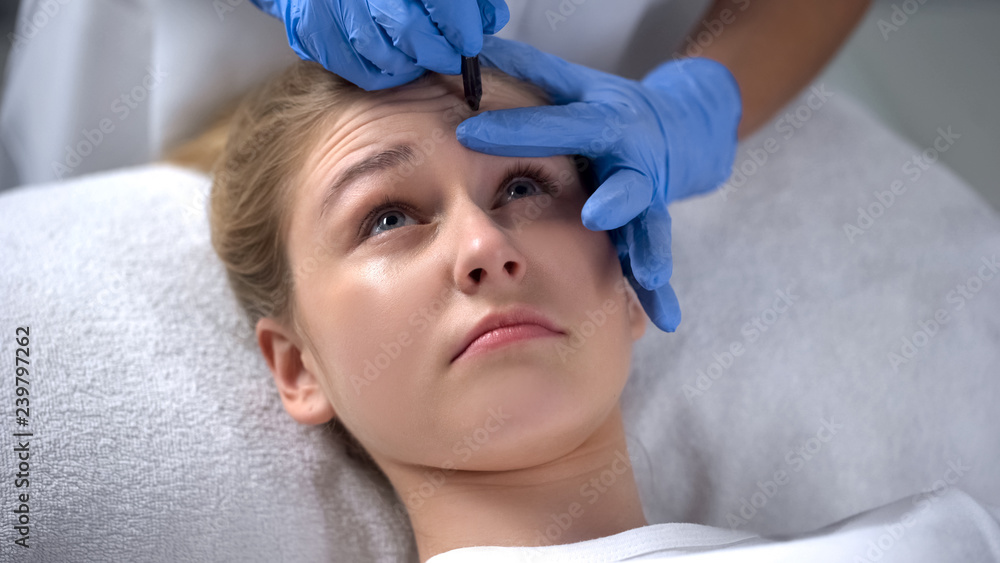 Beautician marking deep forehead wrinkles on clients face, beauty procedures Beautician marking deep forehead wrinkles on clients face, beauty procedures
