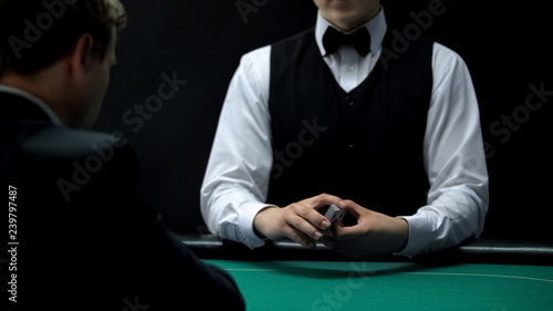 Casino croupier holding deck of cards on green table for client, poker game