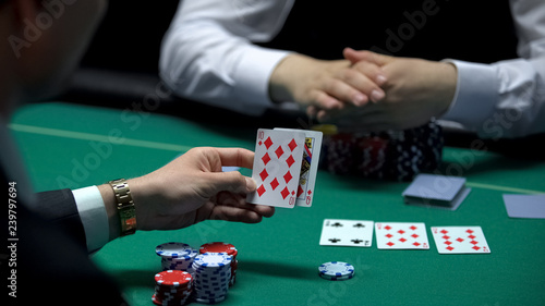Businessman playing poker at casino checking combination of cards, gambling