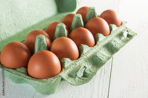 Ten chicken eggs in green carton packaging on white wooden table. photo