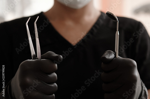 Dentist in black gloves and medical gown holding tools - dental mirror and forceps in clinic. Dentistry, Orthodontics, Stomatology, Dental Care. Close up. selective focus photo