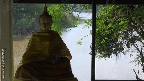 View from inside an Asian pagoda on a flooded river bank. A Buddha statue is partially silhouetted against the fast flowing river.