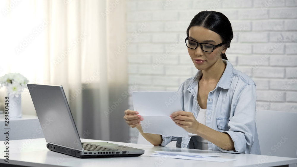 Asian woman in glasses reading letter, subpoena, receipt of correspondence Asian woman in glasses reading letter, subpoena, receipt of correspondence