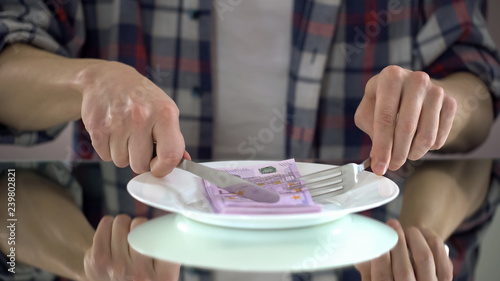 Man eating euro banknotes, wasting money, symbol of consumerism, budget for food