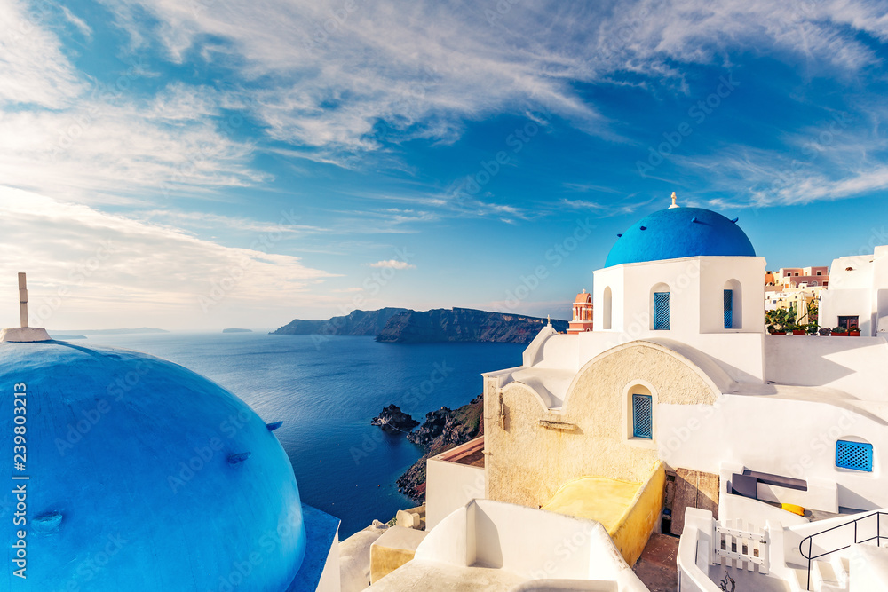 Fototapeta premium Churches in Oia, Santorini island in Greece, on a sunny day with dramatic sky. Scenic travel background.