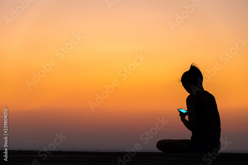 silhouette of young woman using smartphone at sunset