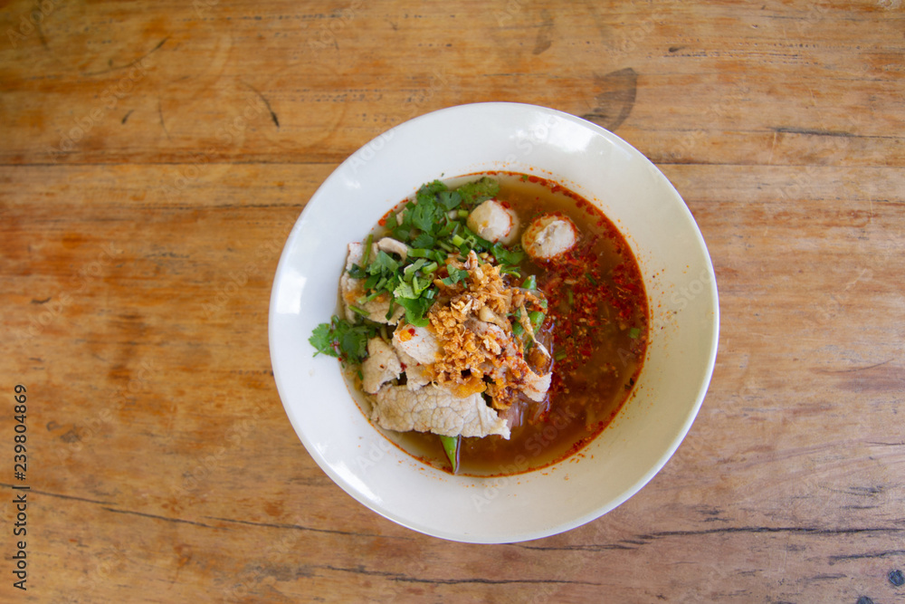 Rice noodle in spicy soup with pork ball, vegetable and pork serving on wooden desk in canteen Rice noodle in spicy soup with pork ball, vegetable and pork serving on wooden desk in canteen