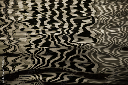 Waves on the water forming stripes similar to the texture of velvet, the alternation of gold and black stripes and waves. photo