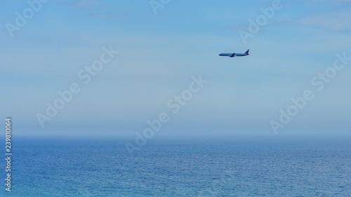 Silhouette of a plane flying against a clean blue sky over the ocean . copy space for text