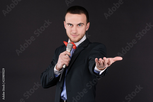 Handsome Master of ceremonies in black suit holding microphone in hand on black background. Showman, tv