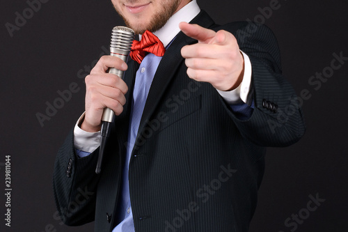 Handsome Master of ceremonies in black suit holding microphone in hand on black background. Showman, tv. closeup photo