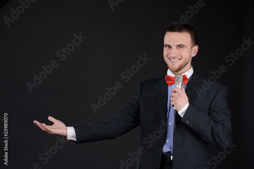 Handsome Master of ceremonies in black suit holding microphone in hand on black background. Showman, tv