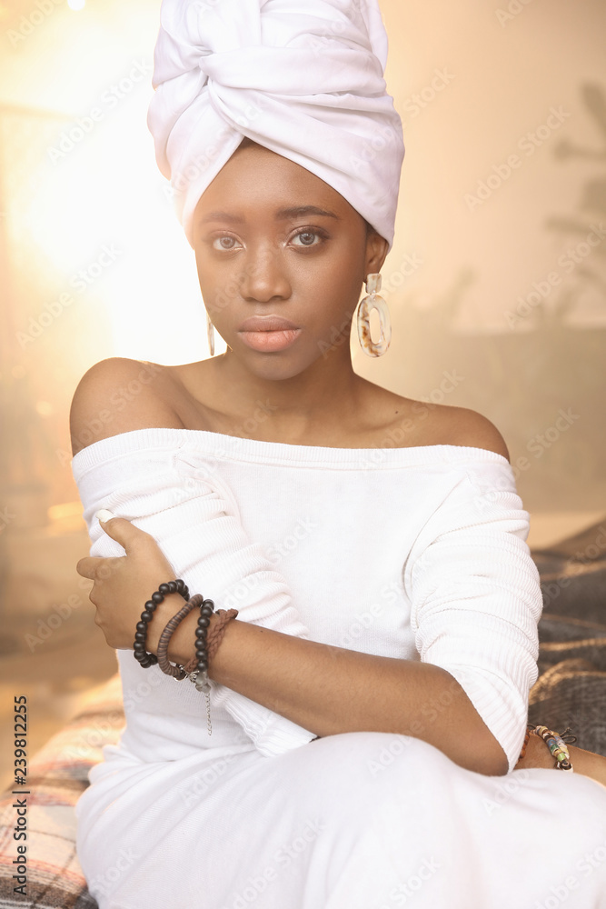 Beauty portrait of young woman dressed in white head tie, white sweater and big earrings, african bracelets. Shiny background. Beauty portrait of young woman dressed in white head tie, white sweater and big earrings, african bracelets. Shiny background.