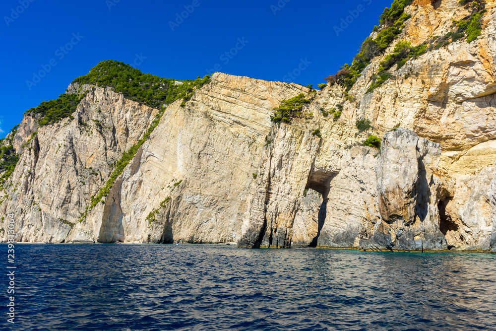 Greece, Zakynthos, Impressive chalk rock cliffs covered by green conifer trees from perfect blue ocean