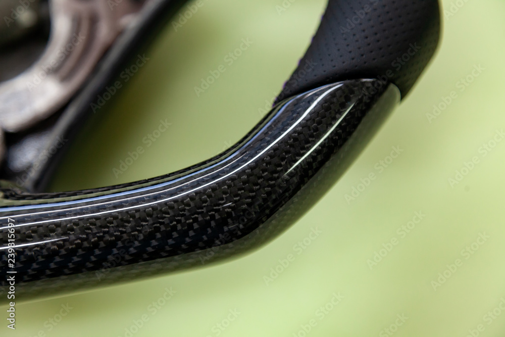 Close-up of a steering wheel detail made of black carbon fiber with perforated leather stitched with purple thread in a design and tuning workshop for vehicle spare parts. Close-up of a steering wheel detail made of black carbon fiber with perforated leather stitched with purple thread in a design and tuning workshop for vehicle spare parts.