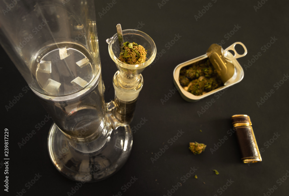 Top view of a crystal bong with marijuana ready to smoke, a tin can with  weed and a elegant lighter on black background. Blur effect on background.  Stock-Foto | Adobe Stock