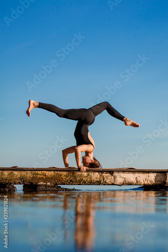 Young woman practicing yoga exercise at quiet wooden pier with city background. Sport and recreation in city rush